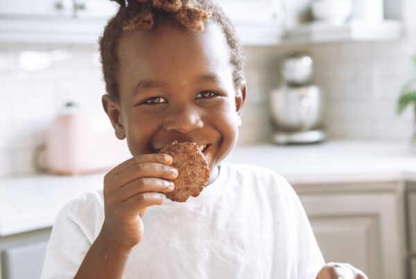 young boy smiling holding cookie to his mouth