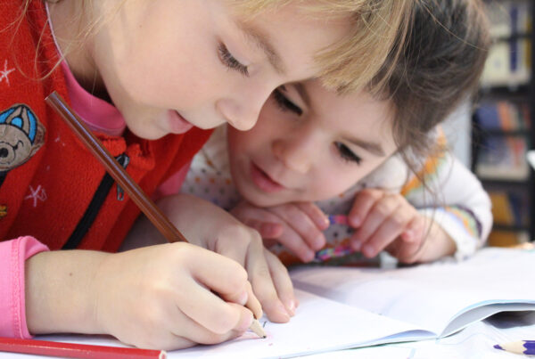 two young girls drawing on a notebook